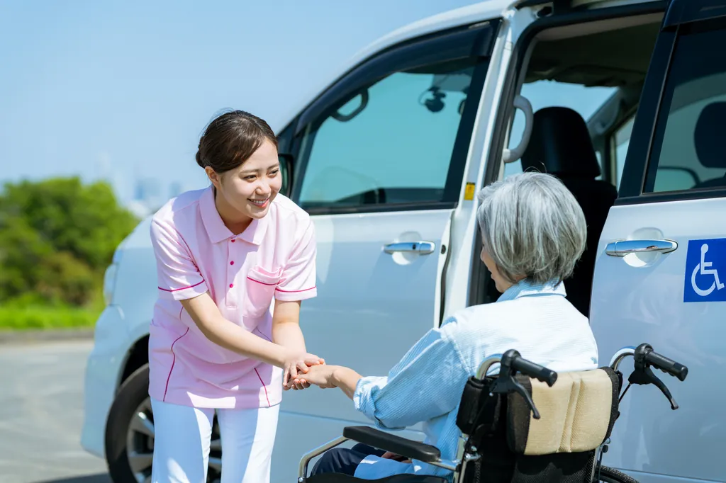 送迎車の前で介護スタッフが車いすの利用者の手を取っている様子