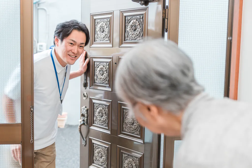 訪問先の玄関で高齢の方に笑顔であいさつする訪問看護師